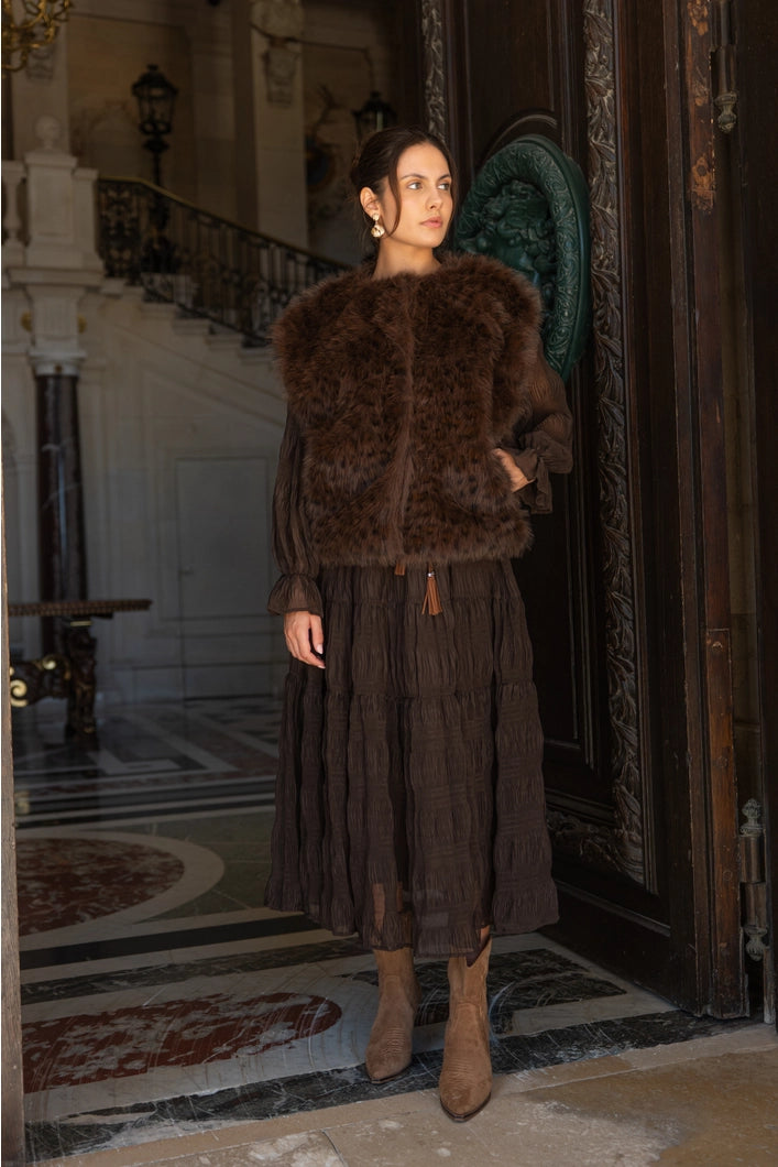 Woman wearing a brown fur coat and dress in an elegant interior setting