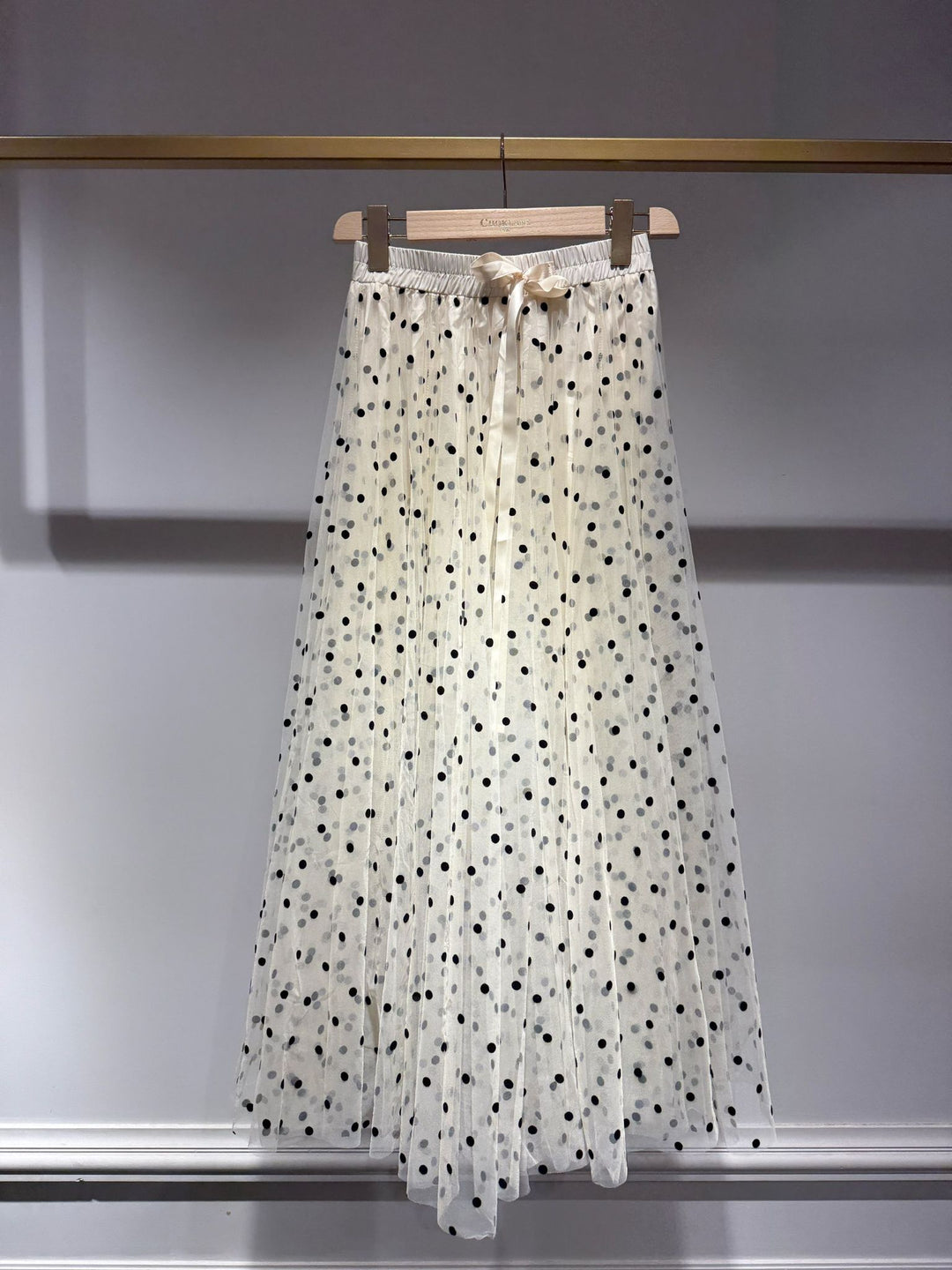 White skirt with black polka dots hanging on a rack against a plain background
