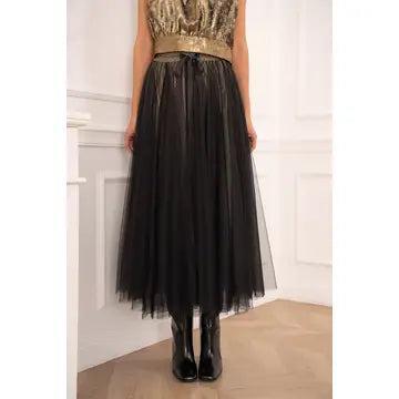 Person wearing a black tulle skirt with a gold top against a white wall.