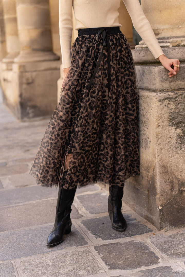 Person wearing a leopard print skirt and black boots standing against a stone wall.