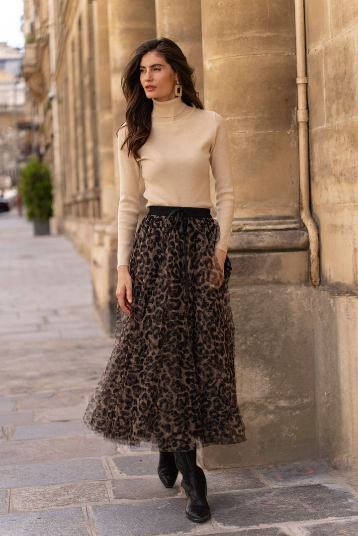 Woman in beige turtleneck and leopard print skirt walking on a street.