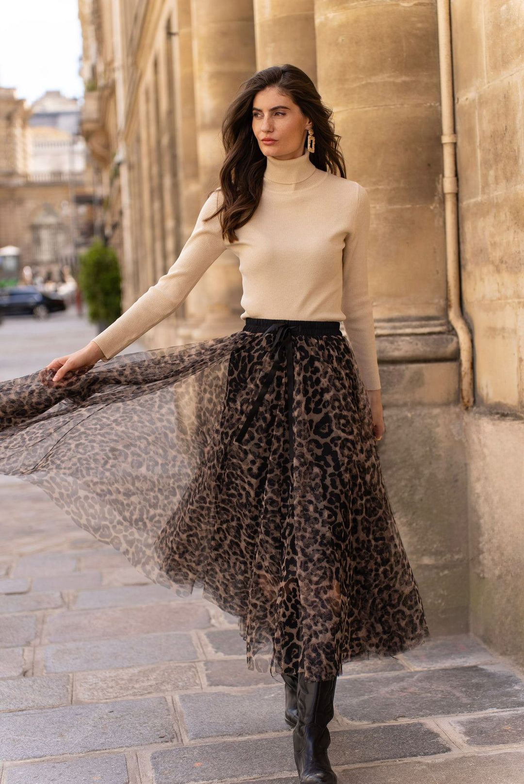 Woman in beige top and leopard print skirt standing on a street.