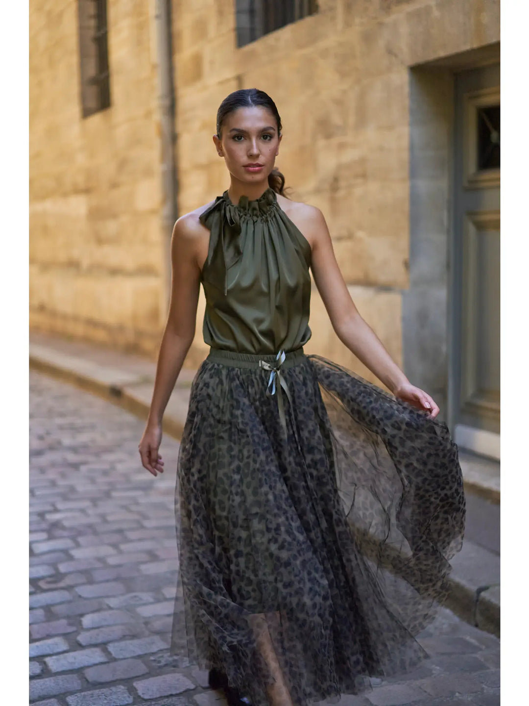 Woman wearing a green halter top and leopard print skirt walking down a stone alleyway.