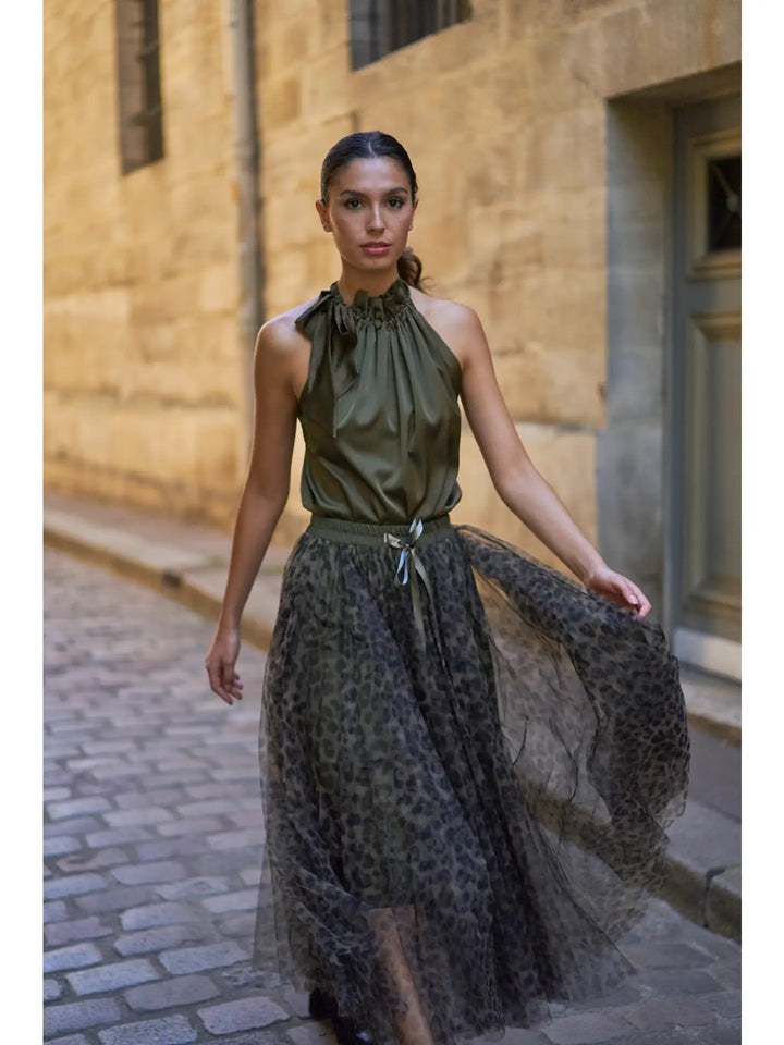 Woman wearing a green halter top and leopard print skirt walking down a stone alleyway.