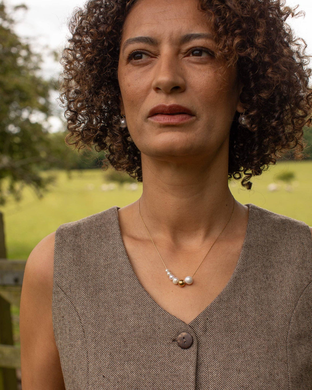 Woman wearing a brown sleeveless top with a necklace in an outdoor setting