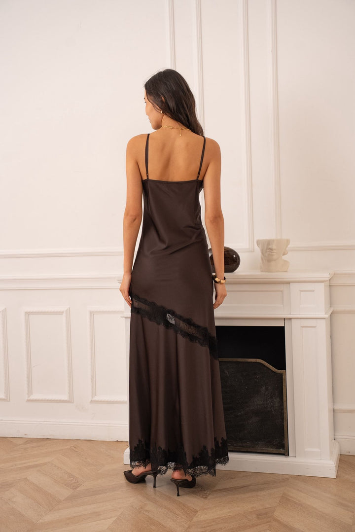 Woman in a brown slip dress standing in a room with a fireplace.