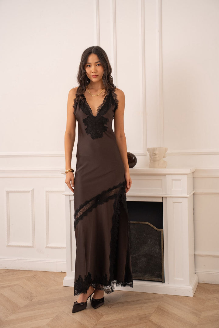 Woman wearing a dark brown evening gown with ruffled details in a room with white walls and a fireplace.
