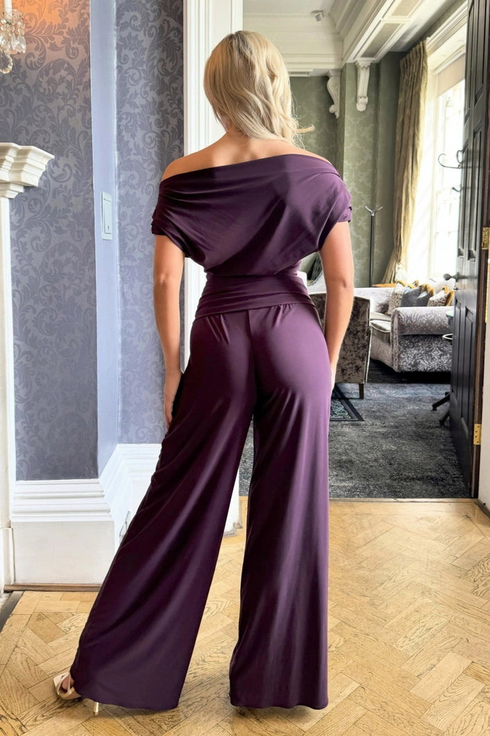 Woman wearing a purple off-shoulder jumpsuit in an elegant room.