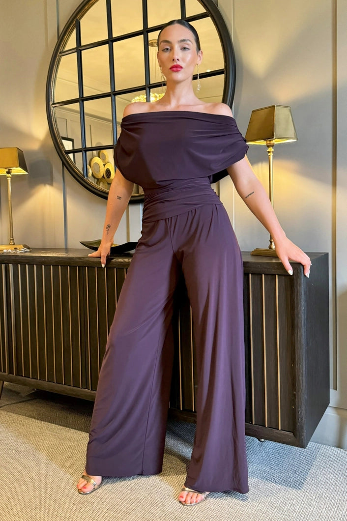 Woman in a purple outfit standing in an elegant interior setting with lamps and a mirror.