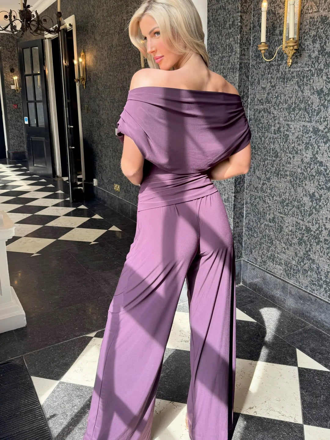 Woman in a purple off-shoulder dress standing in an elegant hallway.