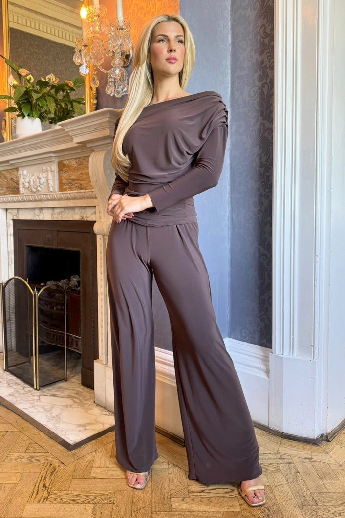 Woman in a brown outfit standing in a room with a fireplace and decorative elements.