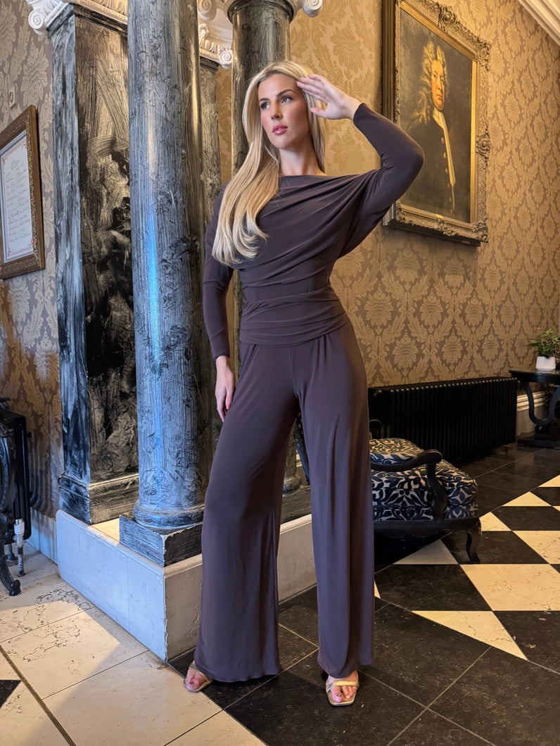 Woman in a dark purple jumpsuit standing in an elegant room with patterned wallpaper and checkered floor.