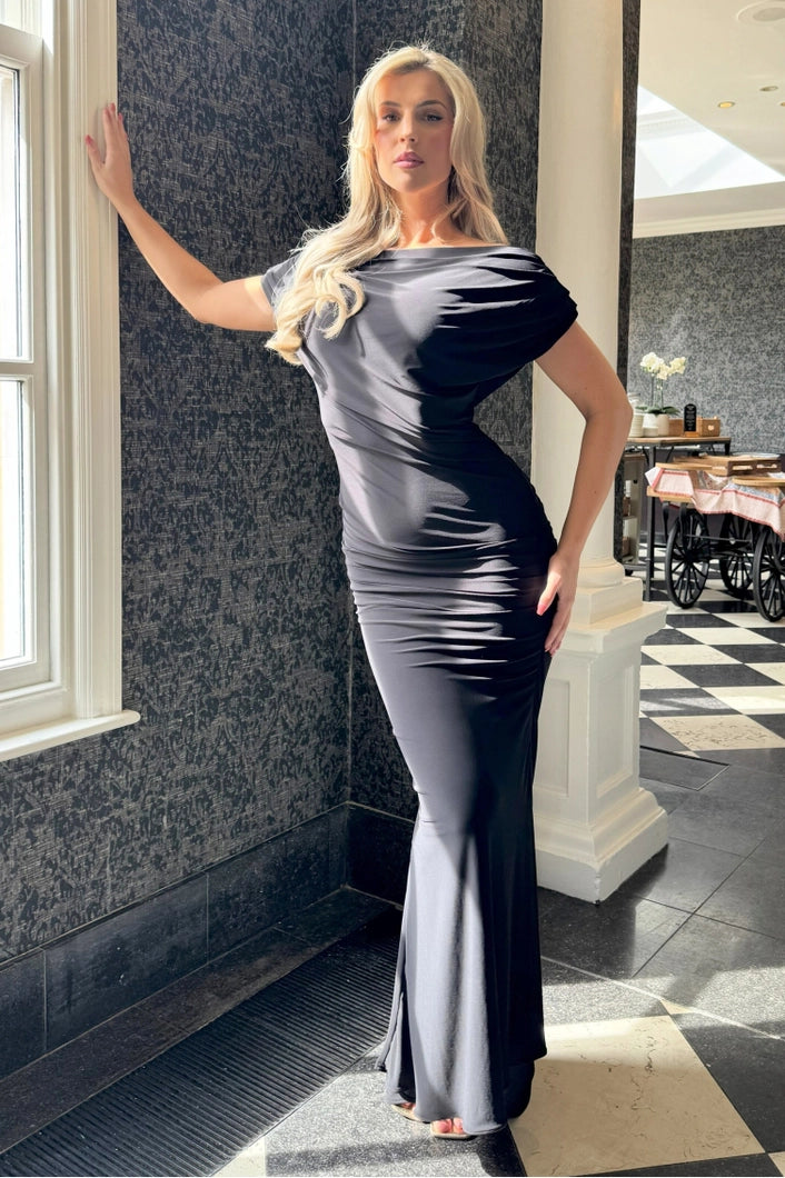 Woman in a gray evening gown standing indoors with a decorative wall and floor in the background.