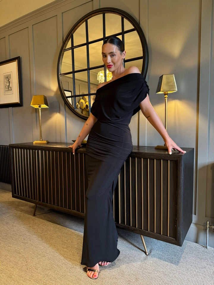 Woman in a black dress posing in a stylish interior setting with a round mirror and lamps.