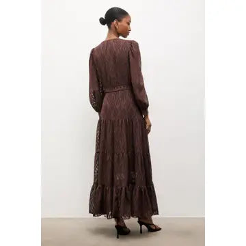 A woman wearing a long-sleeved, dark brown lace maxi dress, shown from the back against a plain white studio background.
