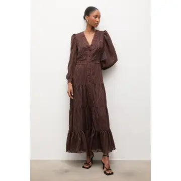 A woman modeling a dark brown, long-sleeved midi dress with a V-neckline, button-up front, and tiered ruffle hem, standing against a plain white wall.