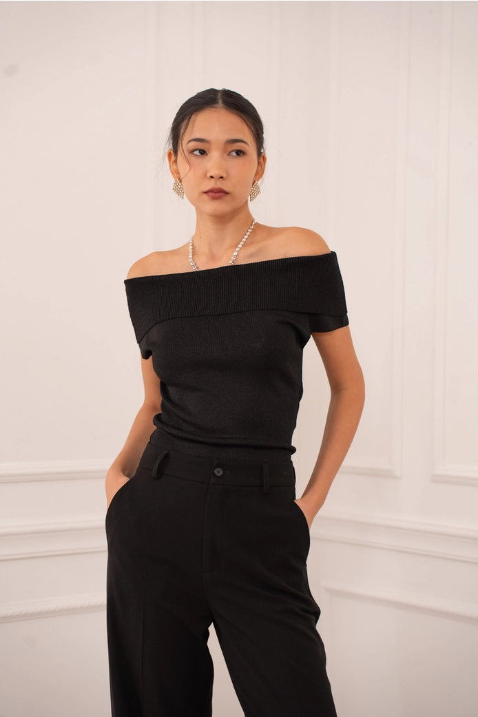 Woman wearing a black off-shoulder top and black pants against a white background