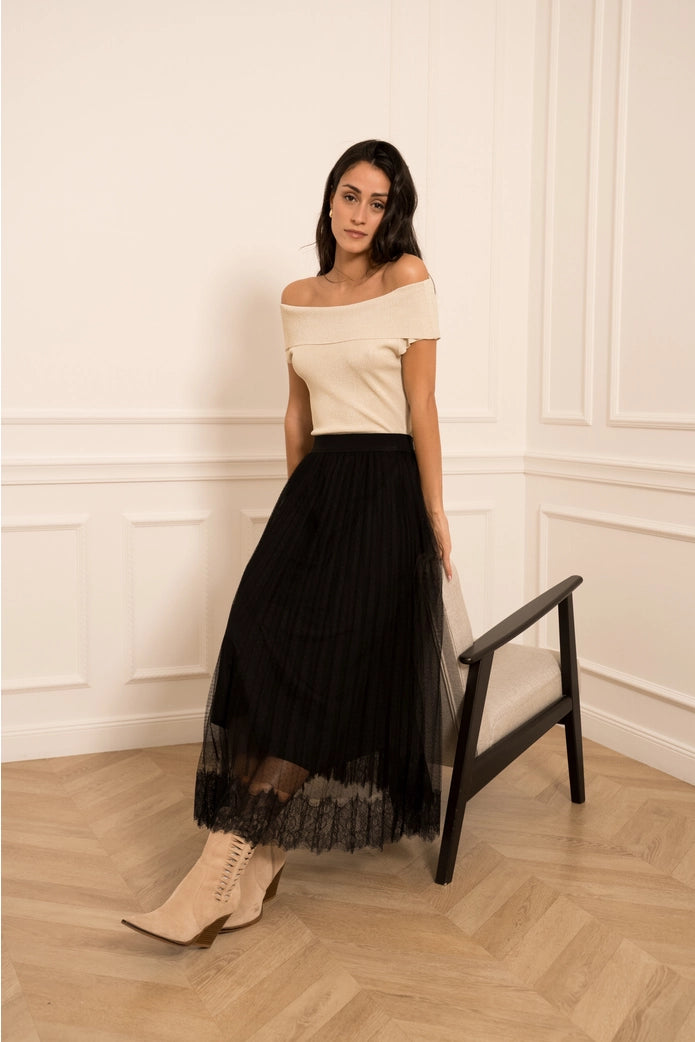 Woman wearing a white off-shoulder top and black tulle skirt in an elegant room.