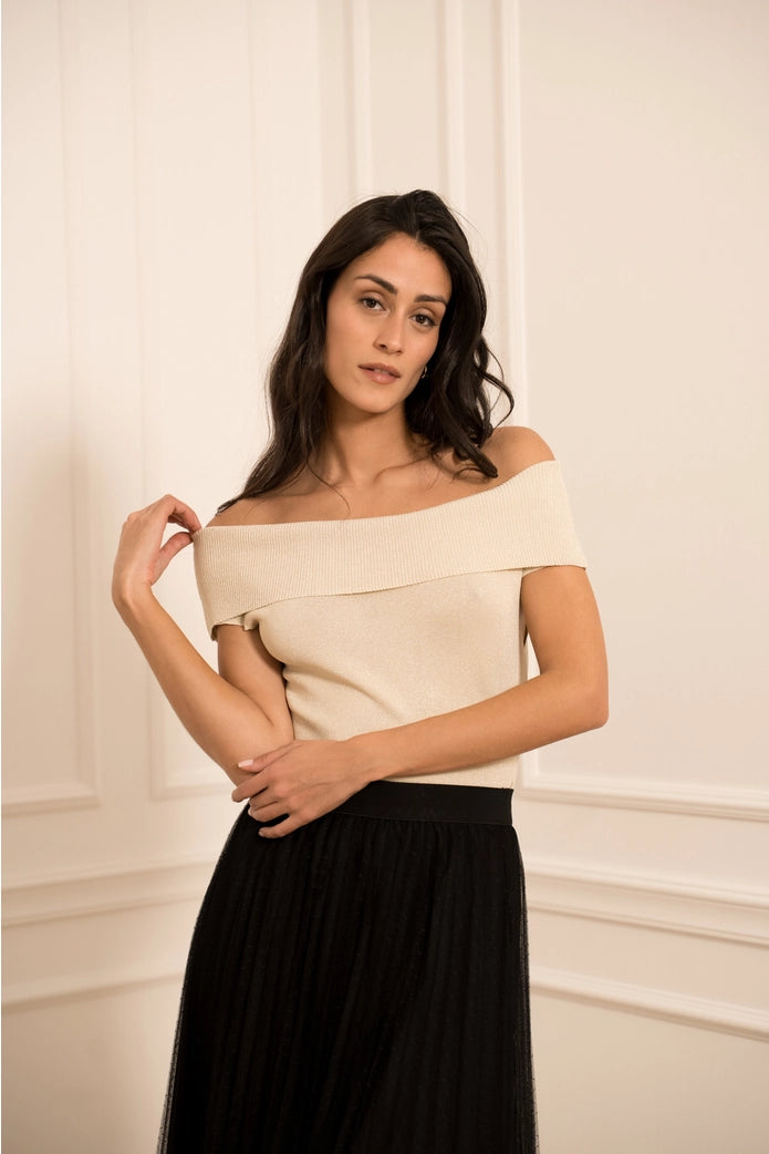 Woman wearing a beige off-shoulder top and black skirt against a neutral background