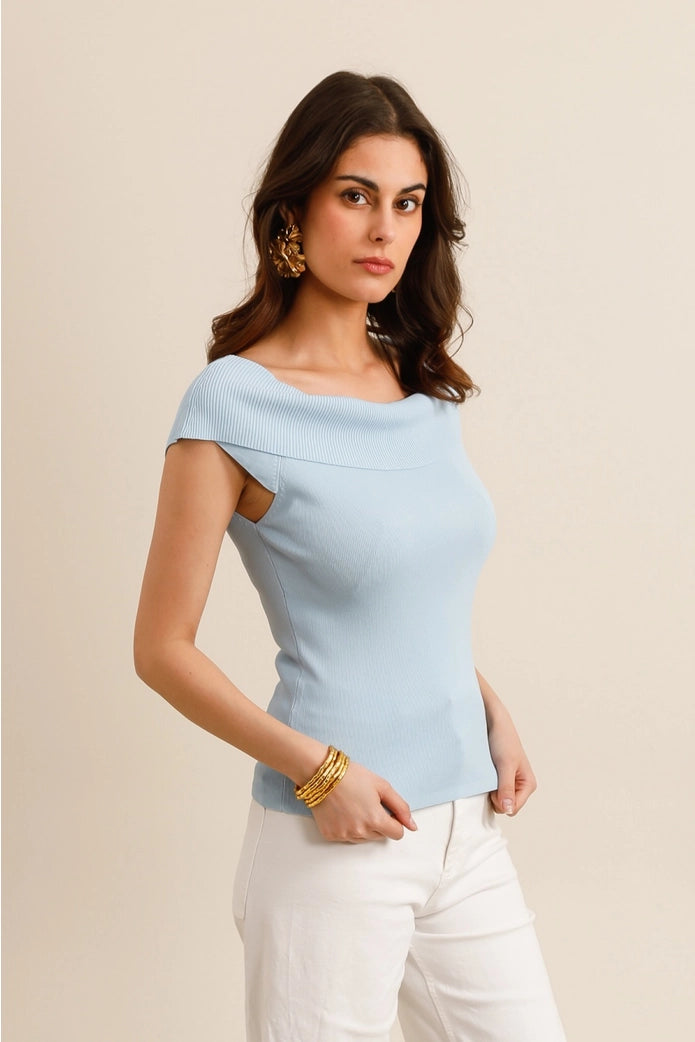 Woman wearing a light blue top with cut-out shoulders against a beige background