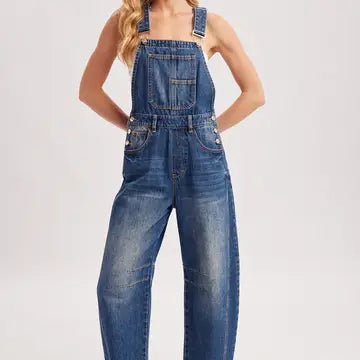 A model wearing blue denim overall jumpsuit with wide legs, photographed against a plain light gray studio background.