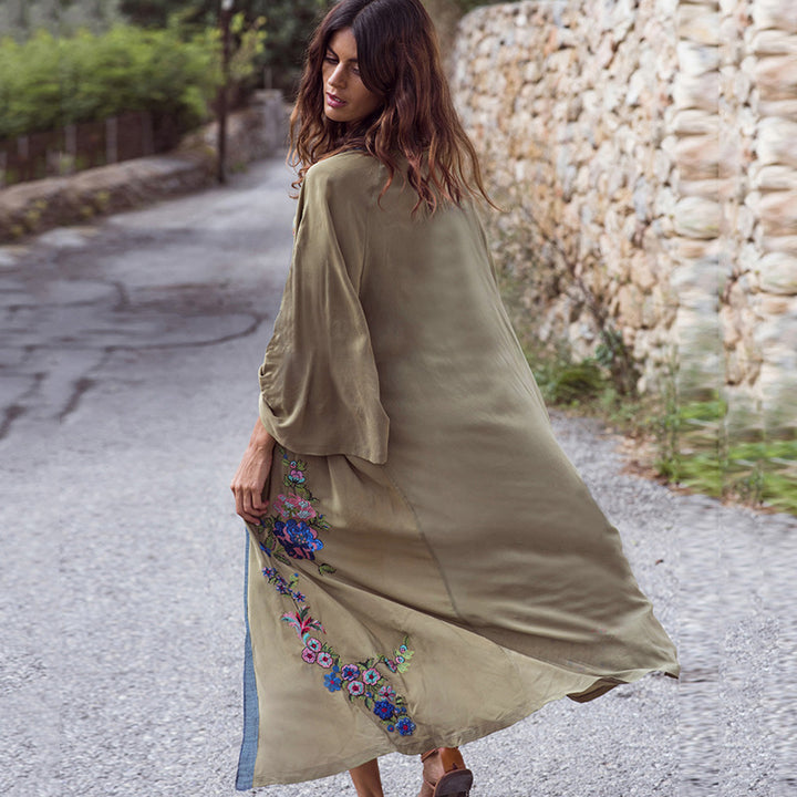 Woman wearing a long, embroidered dress walking on a stone path.