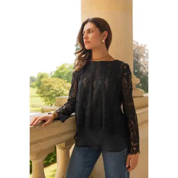 Woman wearing a black lace top and blue jeans standing outdoors.