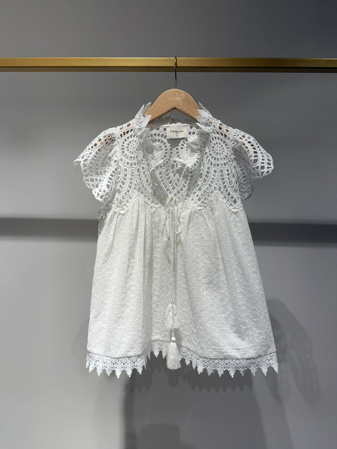 White lace blouse on a hanger against a gray background
