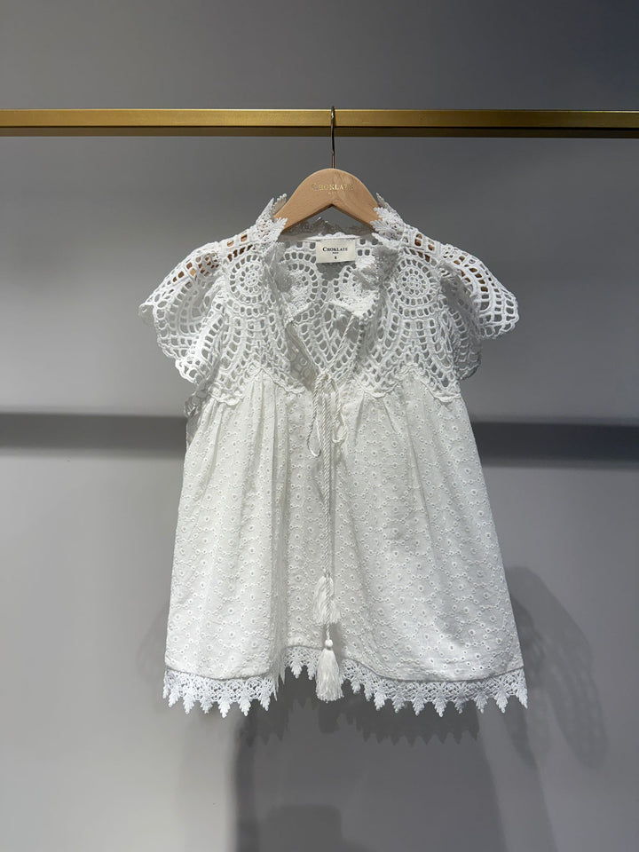 White lace blouse on a hanger against a gray background