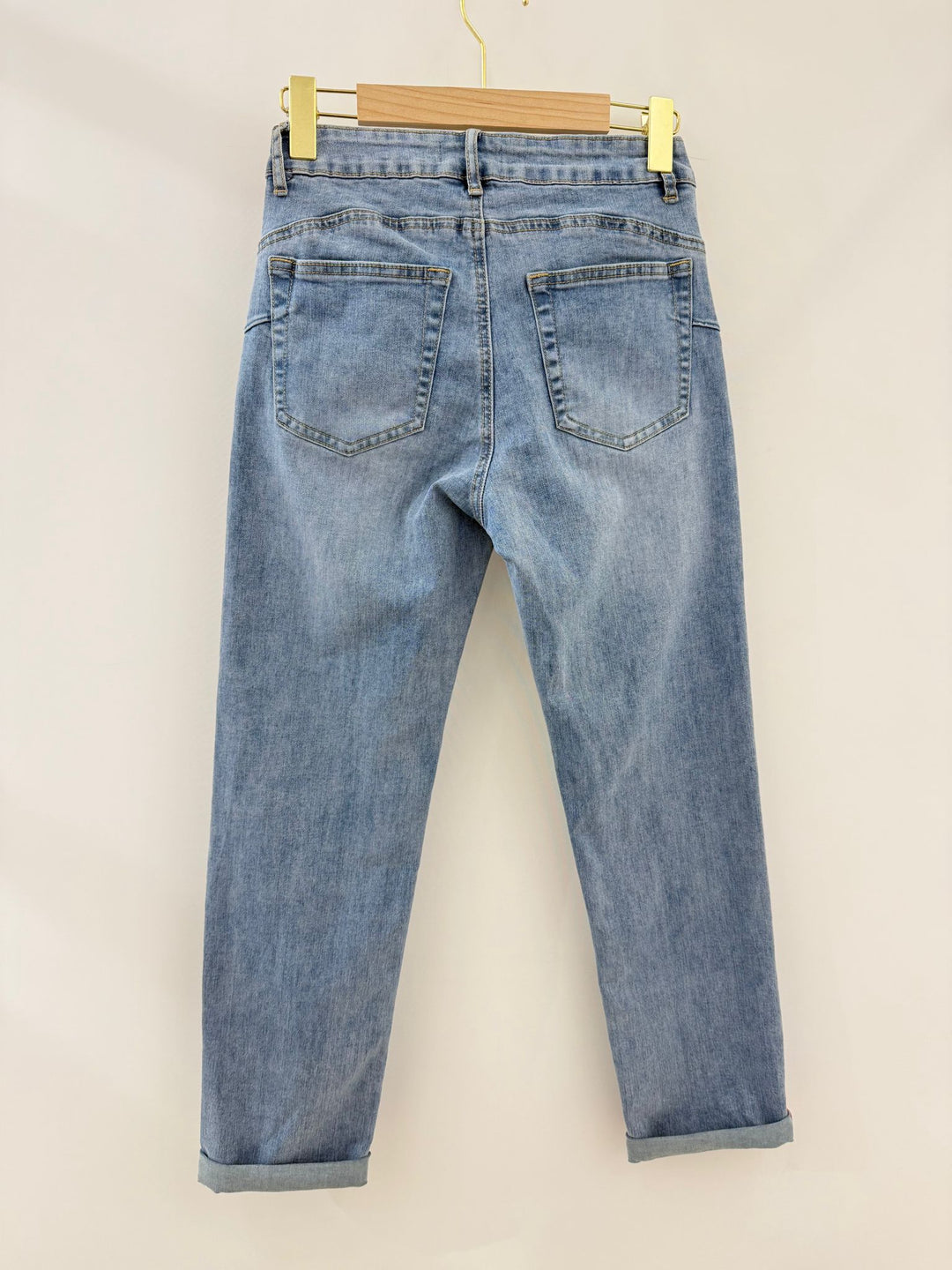 Blue jeans hanging on a wooden hanger against a beige background