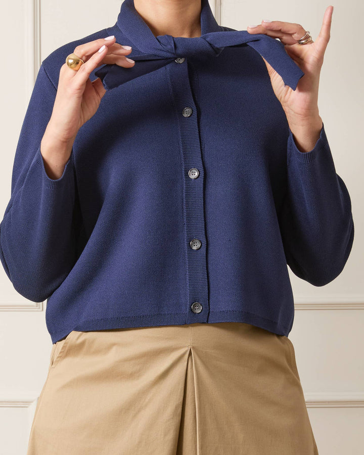 Navy blue cardigan with a bow detail worn by a person, against a neutral background