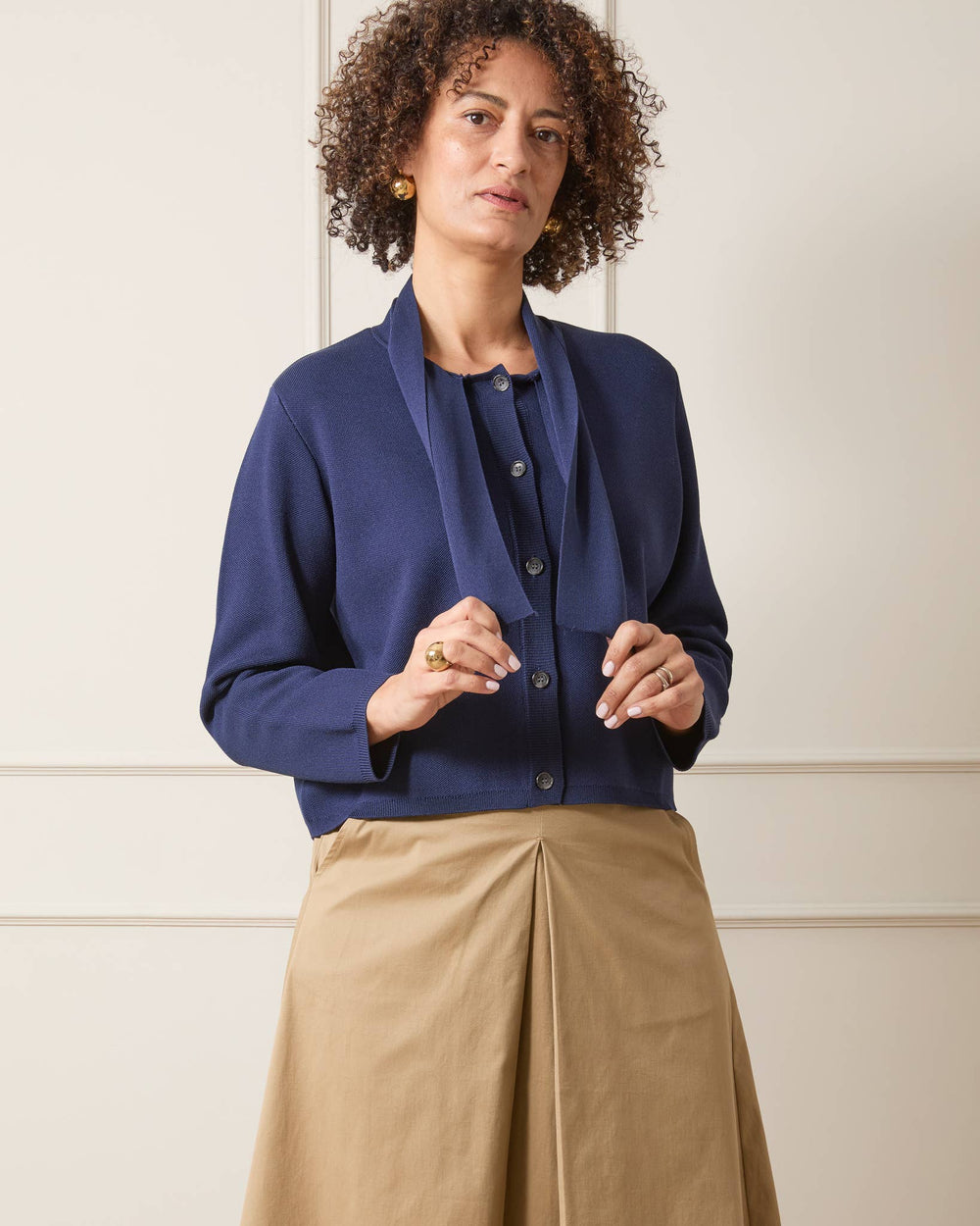Woman wearing a blue blazer and beige pants against a white wall