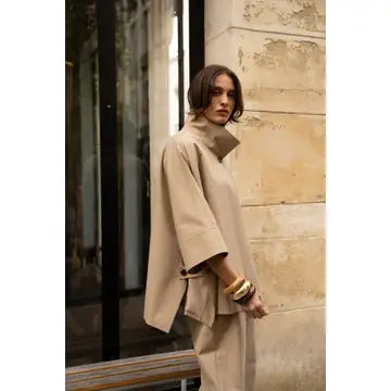 Woman in a beige outfit standing against a stone wall.
