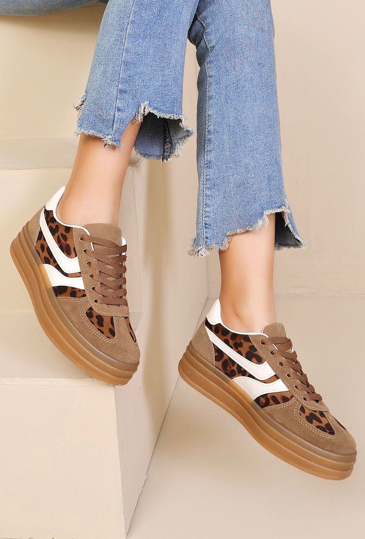 Brown sneakers with leopard print details worn with blue jeans on a beige background