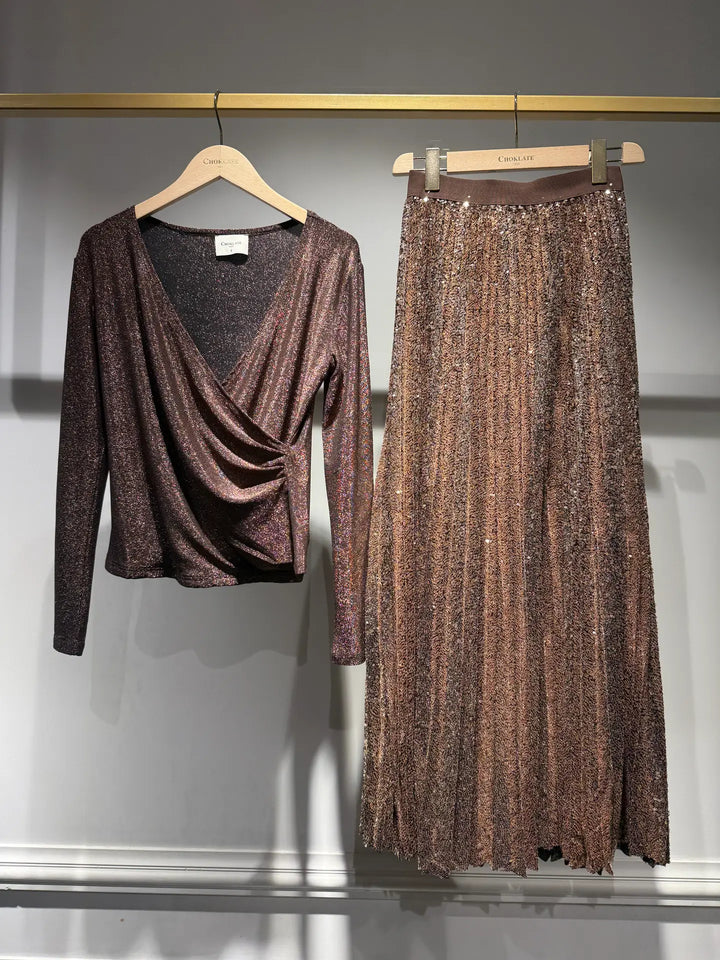 Shiny long-sleeve top and skirt on hangers against a gray background