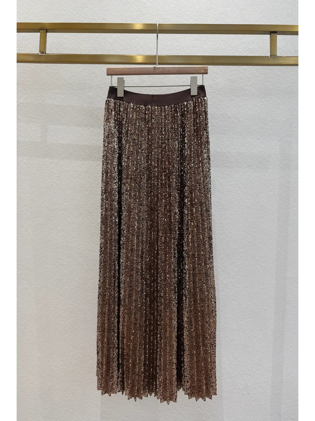 Brown pleated skirt hanging on a rack against a white wall