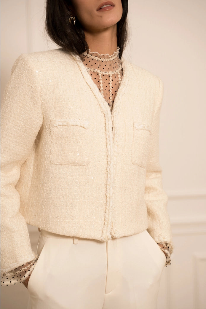Woman wearing a cream-colored blazer with lace details on a plain background