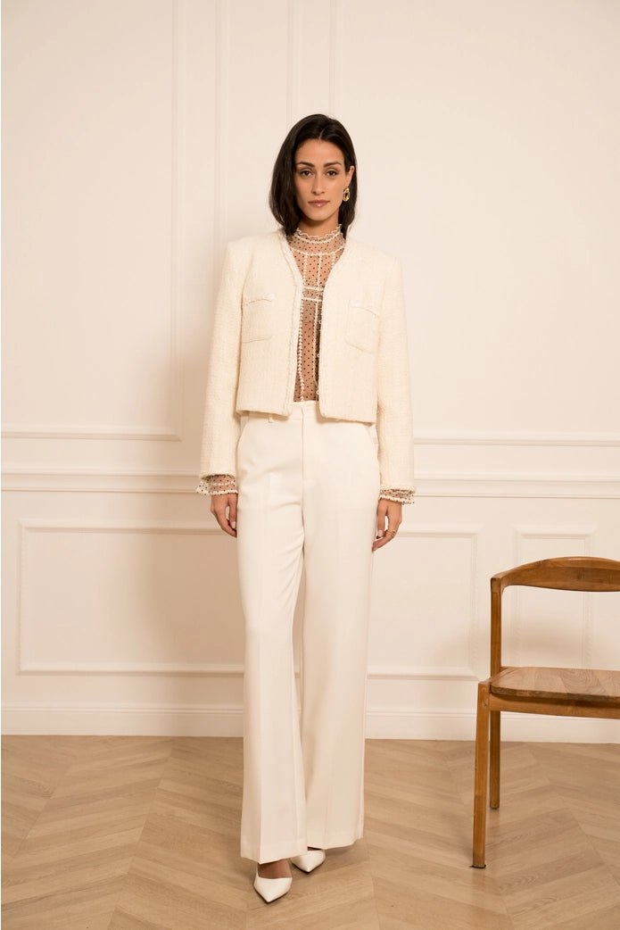 Woman in a white outfit standing in a room with wooden floor and chair.