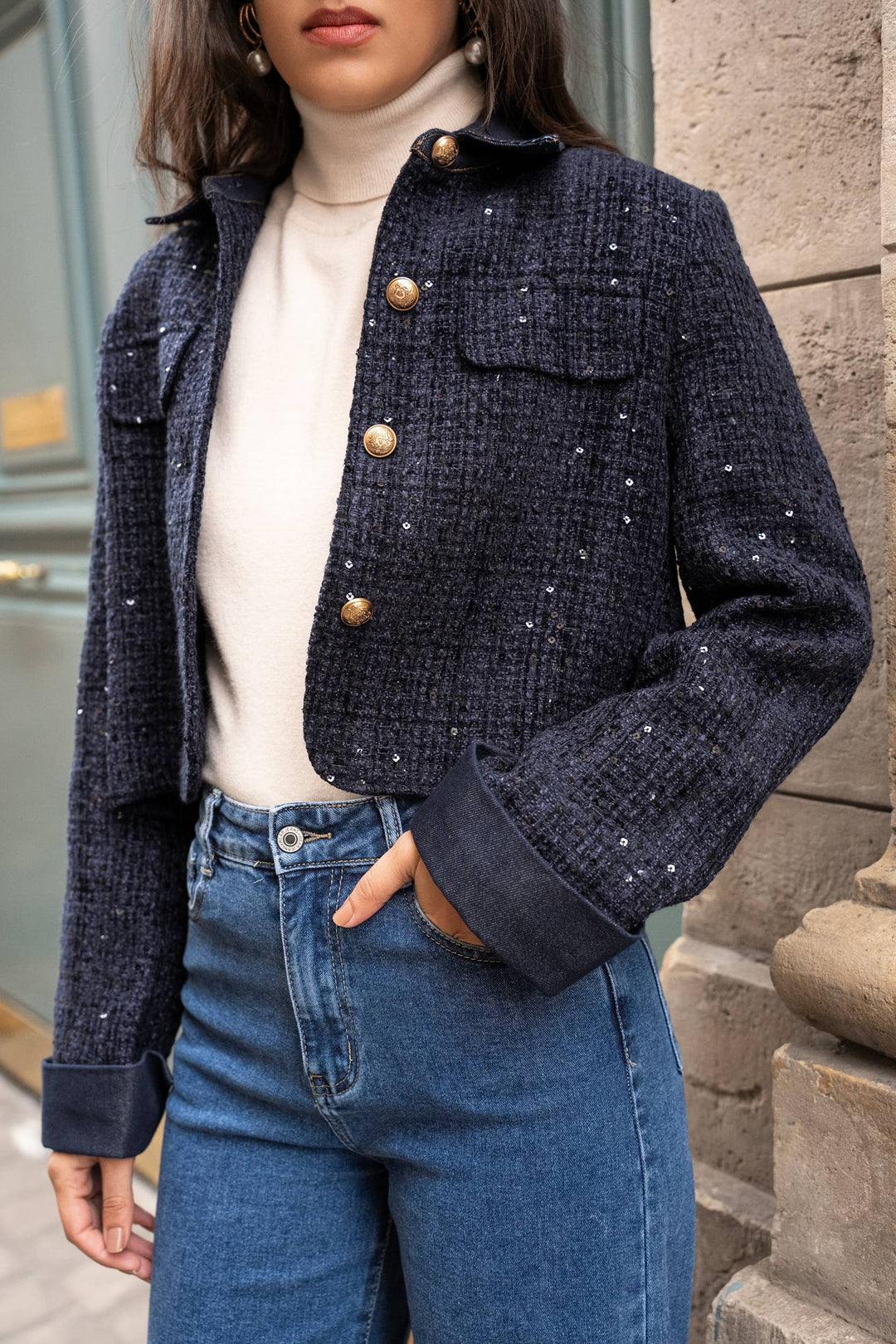 Person wearing a navy blue tweed jacket with gold buttons, white turtleneck, and blue jeans.