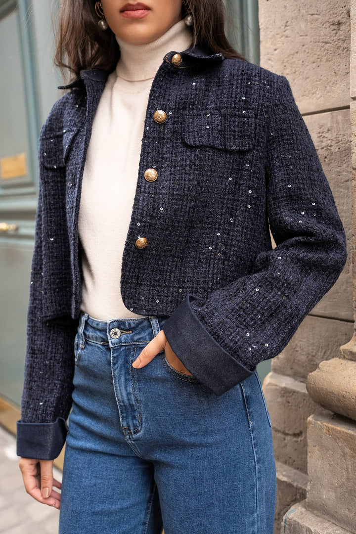 Person wearing a navy blue tweed jacket with gold buttons, white turtleneck, and blue jeans.