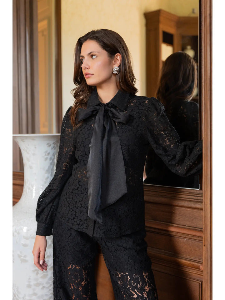 Woman wearing a black lace outfit with a bow tie in a room setting.