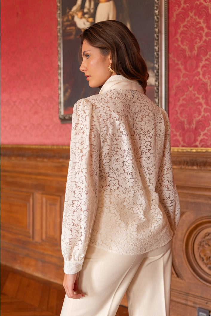 Woman wearing a beige lace blouse in an elegant room with red walls and decorative elements.