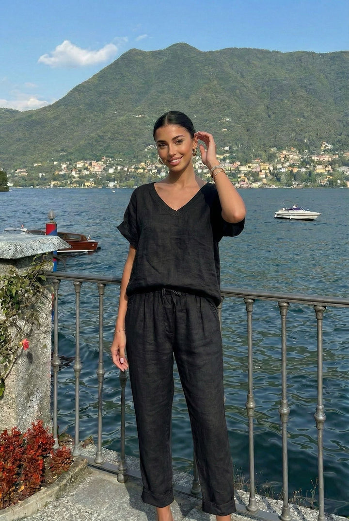 Woman in black outfit standing by a lakeside with mountains in the background