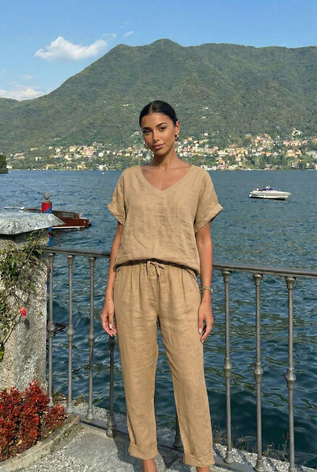 Woman in beige outfit standing by a lakeside with mountains in the background