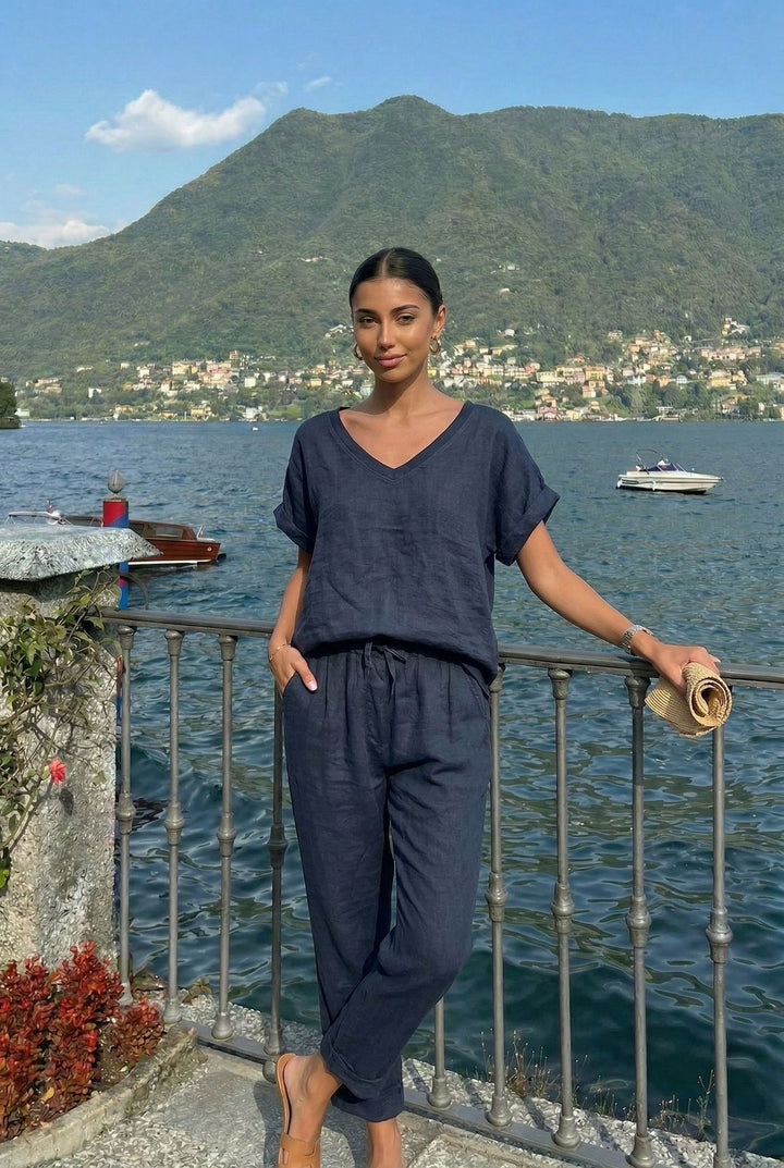 Woman in a navy blue outfit standing by a railing with a scenic view of water and mountains.