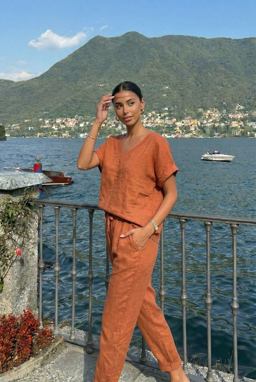 Woman in an orange outfit standing by a lakeside with mountains in the background