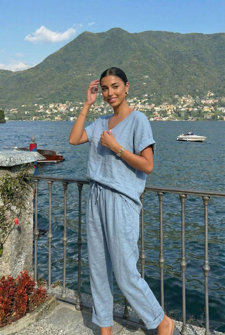 Woman in a blue outfit standing by a lakeside with mountains in the background