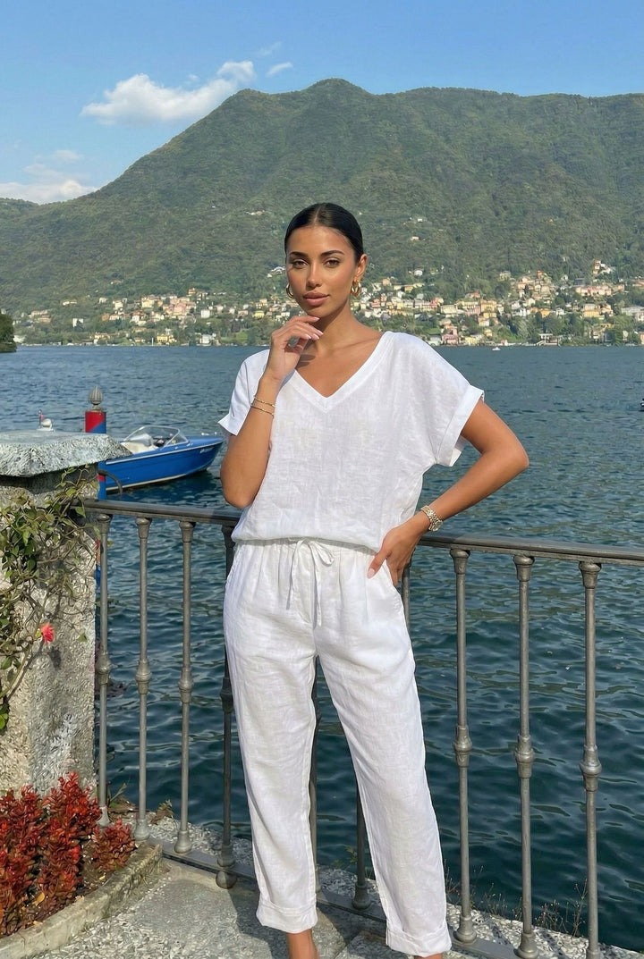 Woman in a white outfit standing by a scenic lakeside with mountains in the background