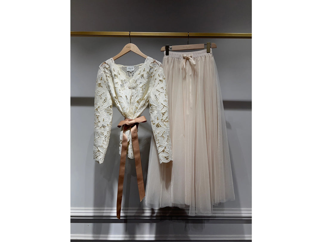 Lace top with a brown ribbon and tulle skirt on hangers against a gray background