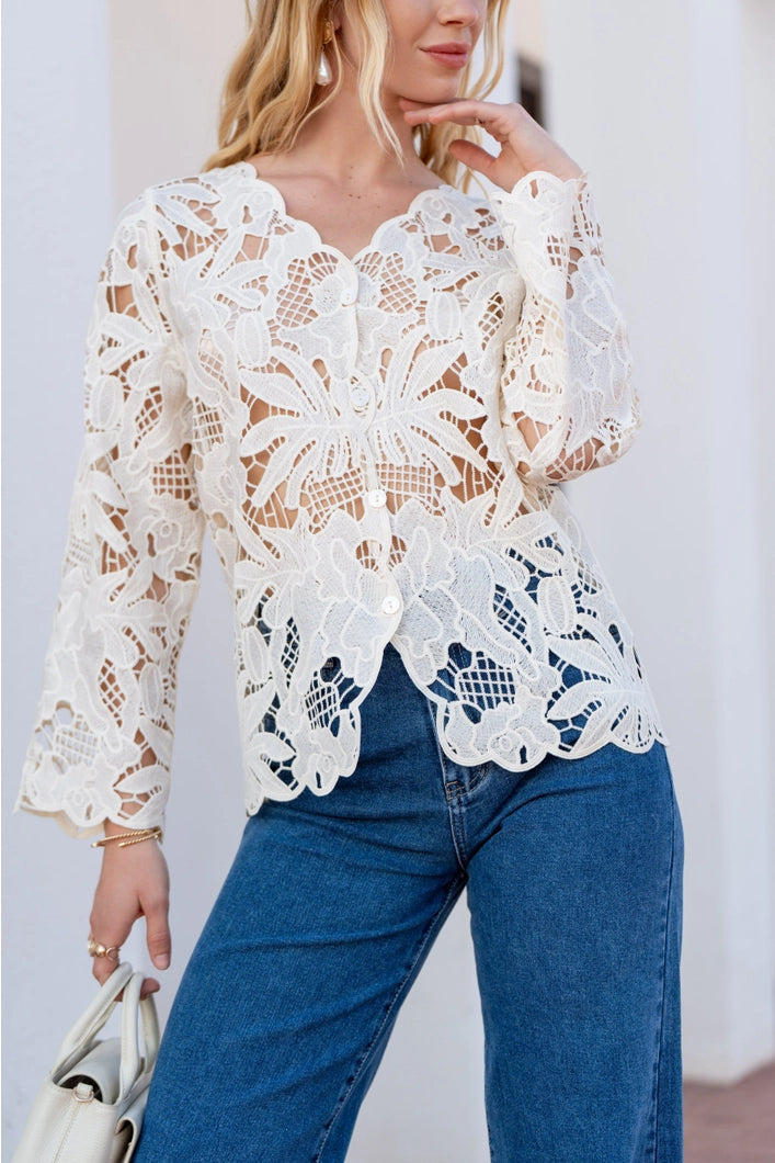 Woman wearing a white lace top and blue jeans against a neutral background